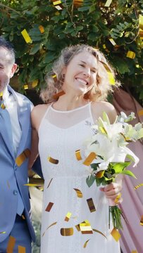 Vertical video: Couple posing in garden, confetti releasing above while holding bouquet for wedding