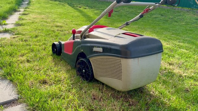 Electric Lawn Mower on Green Grass Next to Stone Paving Path in Garden, Yard Maintenance