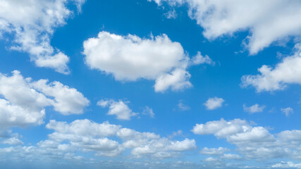 Fototapeta premium A bright blue sky filled with scattered white cumulus clouds of various sizes, creating a peaceful and expansive atmosphere typical of a clear, sunny day with light weather conditions.