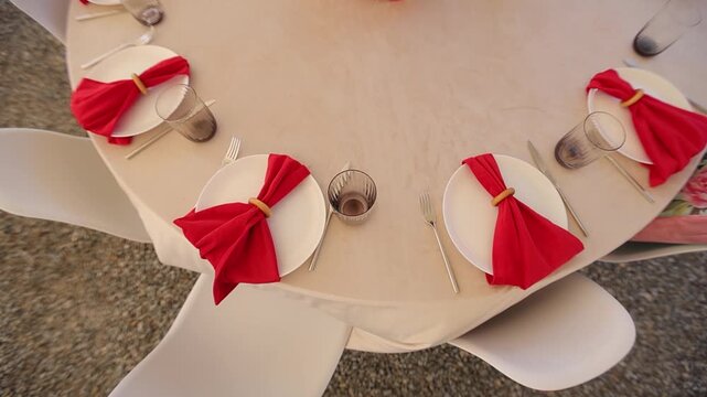 Round table with white tablecloth and empty plates, forks, and glasses, decorated for the holiday. Top view of the table with red napkins in restaurant.