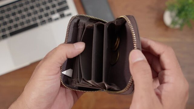 Hands holding an empty wallet with a small amount of coins remaining, representing economic challenges, poverty, and personal finance problems.
