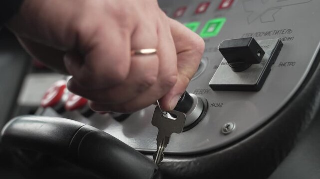 Tram driver turns metal key and starts the vehicle. The car's dashboard features sensors and illuminated buttons.