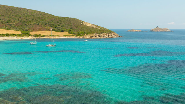Turquoise sea and sailboats anchored in a calm bay with a rugged coastline and distant islands, offering a serene travel and tourism destination in North Corsica.