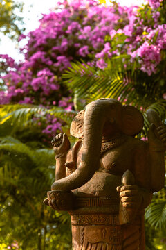 Stone statue of Lord Ganesha surrounded by vibrant pink bougainvillea flowers in a tropical garden.

Ancient Hindu deity sculpture at the Po Nagar Cham Towers in Nha Trang, Vietnam.