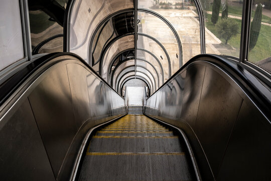 Escalator descent curves through interior architecture, where tunnel reflection, railing and symmetry guide transit inside a station