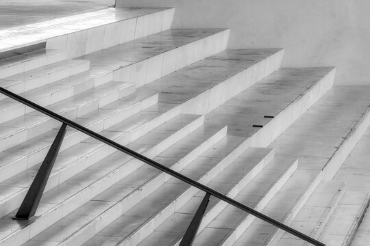 Minimal stairs fade through bright interior architecture, with railing, geometry, shadow and concrete surfaces forming abstract access