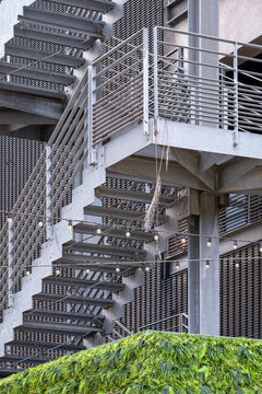 Metal stairs wrap industrial architecture, with railing, facade, platform and geometry lifting an exterior structure above greenery
