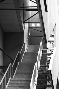 Monochrome stairs rise inside industrial architecture, with railing lines, shadow, concrete texture and interior structure shaping vertical design