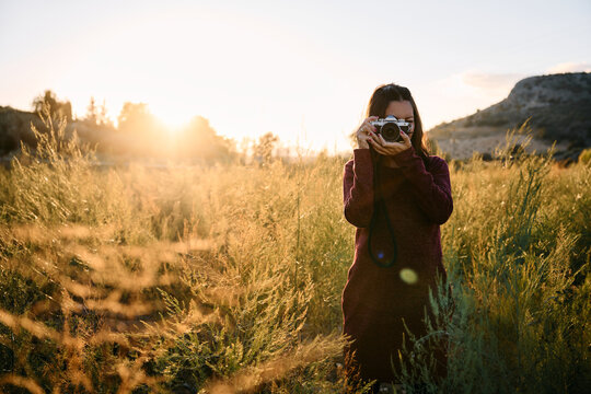Woman shooting with a vintage camera in a golden field