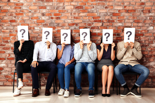 Group of diverse people sitting in a row holding question mark signs over their faces expressionless