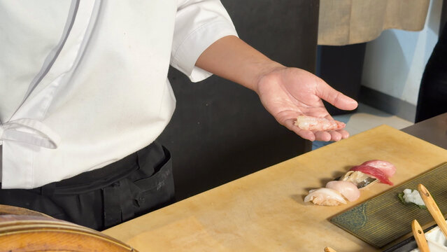 Sushi Chef Holding Fresh Shrimp Nigiri Over Wooden Omakase Counter