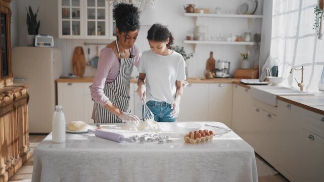 African american woman and her teen daughter cooking dinner at home, baking pie. Happy black lady and pretty girl making dough for cookies, cozy home interior of modern kitchen, calm family weekend