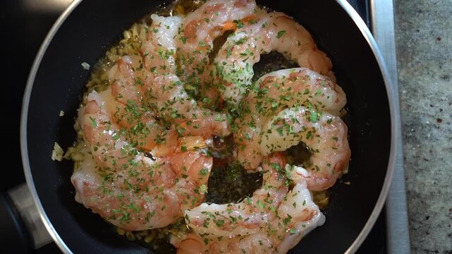 Shrimp saut ing in olive oil with garlic and parsley in a frying pan on the stove fresh, homemade seafood meal preparation