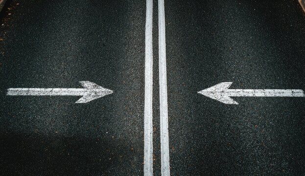 Two white arrows painted on asphalt road pointing towards each other