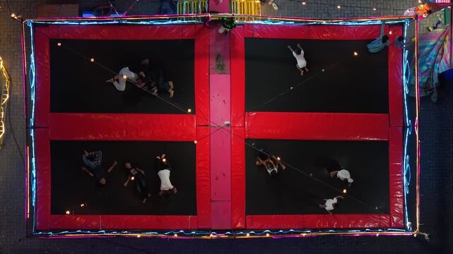 Aerial view of people jumping on large trampolines at the GOR Gelarsena Klaten Night Market with colorful lights at night in Kecamatan Klaten Utara, Jawa Tengah, Indonesia.