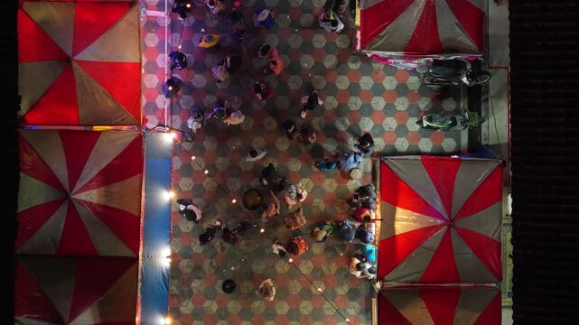 Aerial view of GOR Gelarsena Klaten Night Market with people walking between red and white striped tents at night in Kecamatan Klaten Utara, Jawa Tengah, Indonesia.