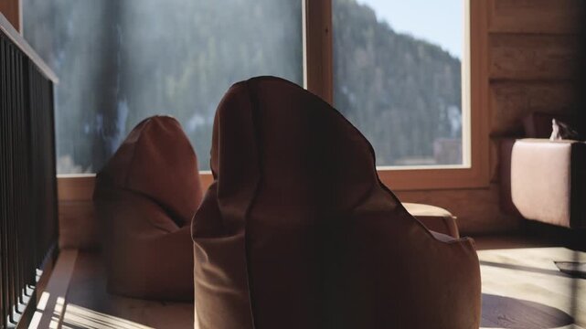 Empty beanbag chairs in a sunny wooden cabin living room with a mountain forest view outside