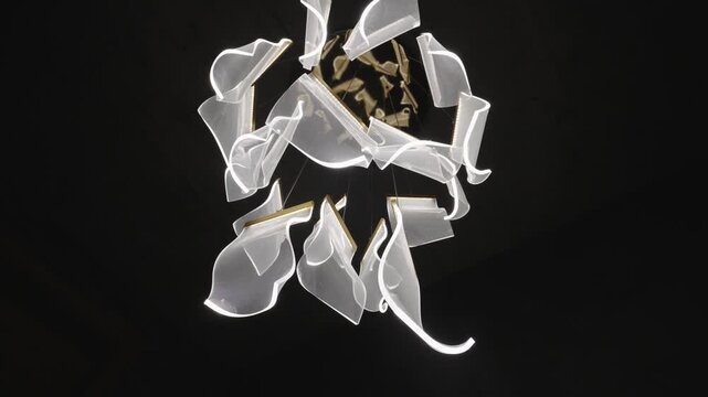 Sculptural led chandelier with wavy acrylic elements gently turning against a dark background