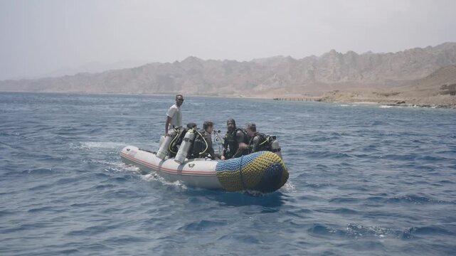 Group of scuba divers in wetsuits navigating a rigid inflatable boat on the open sea
