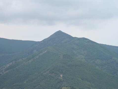 Montagna verde e rigogliosa sotto cielo nuvoloso, con pendii stratificati e atmosfera naturale e silenziosa