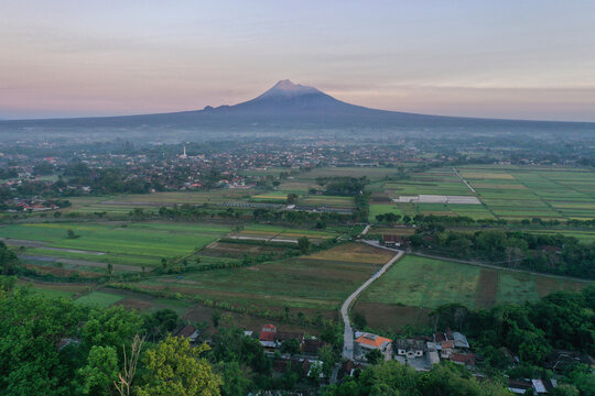 Majestic aerial view of Mount Merapi volcano with traditional village and rice fields at dawn, Yogyakarta, Indonesia.