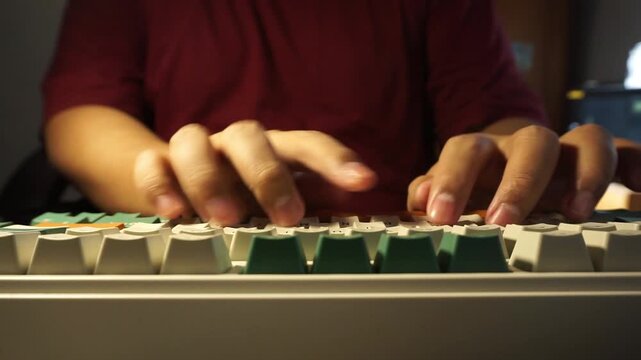 A direct front view from a low angle showing a male person in a red shirt typing rapidly on a mechanical keyboard with colorful keys, framed symmetrically in an indoor setting.