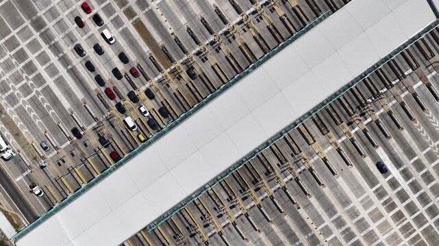Cars queuing in a traffic jam at a toll plaza on a busy highway, paying tolls at the checkpoint before continuing their journey. An aerial perspective of the transportation infrastructure