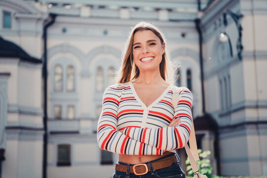 Smiling young woman in striped sweater posing confidently outdoors in a sunny urban setting