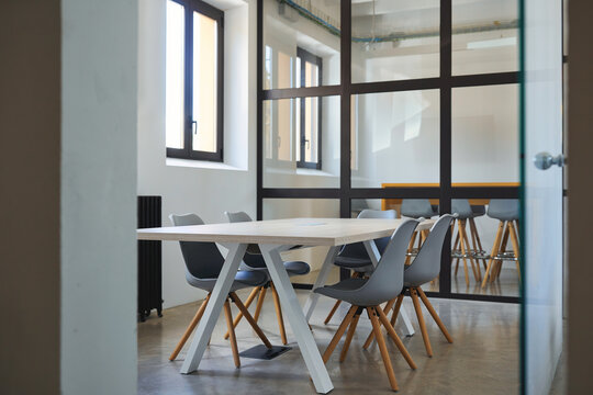 Bright modern meeting room interior with a wooden table, gray chairs, glass partition, large windows, and natural daylight in a contemporary office space.