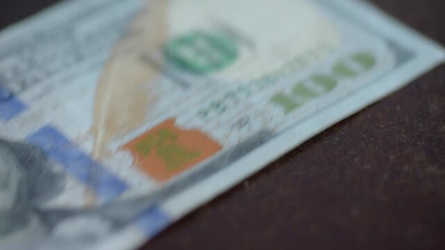 Closeup caucasian finger sliding hundred dollar across table, office worker discreetly pockets bill, quick blur of movement, empty wood surface aftermath, stealthy tension, urgent