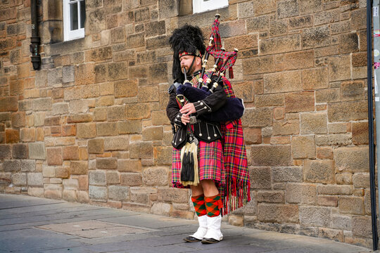 A bagpiper in traditional Scottish attire in front of a historic stone wall on the famous Royal Mile in Edinburgh, Scotland