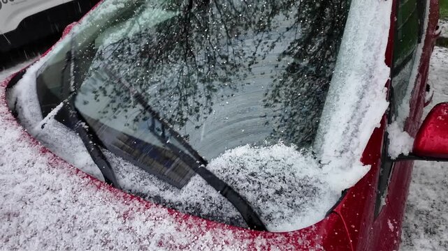 Gros plan sur des petits gr&ecirc;lons qui tombent sur le parebrise d'une voiture rouge. Les essuie glaces les balayent. Boules de glace apr&egrave;s un orage de printemps.