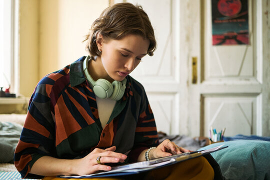 Young adult Caucasian woman studying with notebook and headphones, reviewing notes at home and preparing coursework. Useful for education, online learning, student life marketing