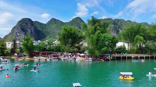 Crystal Clear Emerald River with Small Boats, Karst Mountains and Village in Back