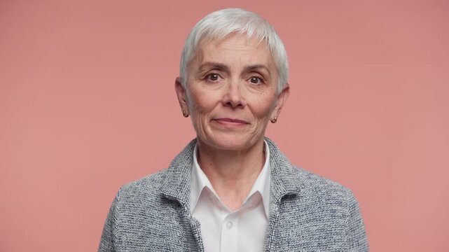 Senior woman shrugging with uncertain expression on pink
