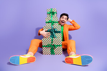 Naklejka premium Happy man in orange outfit sitting with stack of wrapped Christmas gifts celebrating colorful holiday excitement