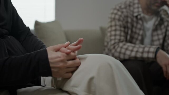 Close up of woman holding napkin and touching golden wedding ring while her spouse sitting near her during family therapy in office
