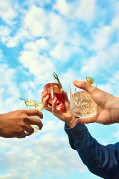 Group toast with red and clear cocktails under sunny sky. Concept of cocktail tasting, private event, spring hospitality, bar promotion and premium social lifestyle.