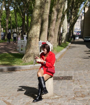 A woman in a red jacket sitting on a stone bollard eating from a takeout bowl on a cobblestone street