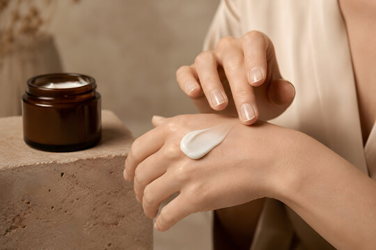 Applying luxury firming cream to hand, close-up of anti-aging skincare application with amber glass jar on travertine podium, premium beauty campaign.