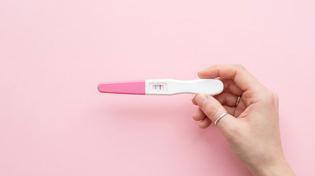 Woman s hand holding a positive pregnancy test with two red lines against a pink background