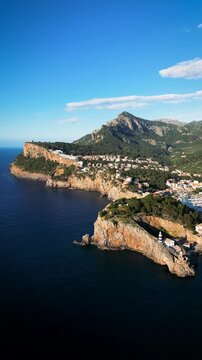 Aerial view of Port de Soller featuring the lighthouse on rugged cliffs with the Tramuntana mountains in Port de Soller, Balearic Islands, Spain.