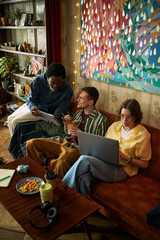 Fototapeta premium Vertical shot of diverse young adults collaborating with laptop and tablet while sitting together, discussing creative project and remote workflow. Ideal for hybrid work, startup teamwork marketing