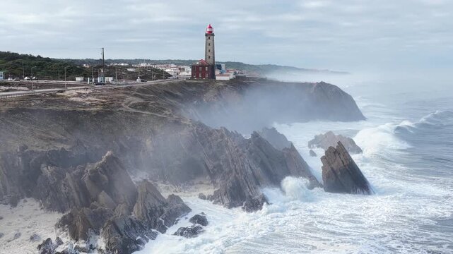 Aerial view of Farol Penedo da Saudade on rocky cliffs with crashing waves and sea spray in Marinha Grande, Leiria, Portugal.