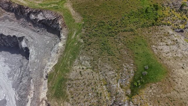 A mining site shows grey rock and soil on one side while the other side is filled with green grass and plants. This scene highlights the differences in land use and vegetation.