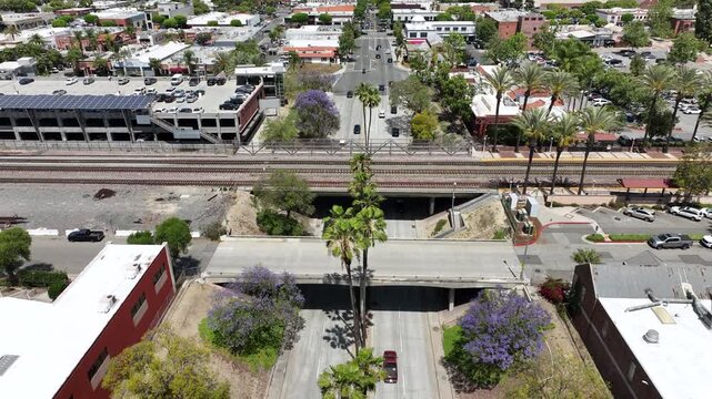 Drone view above Harbor Boulevard in Fullerton capturing busy city traffic and a passenger train passing over the railway bridge on a clear sunny Southern California day.