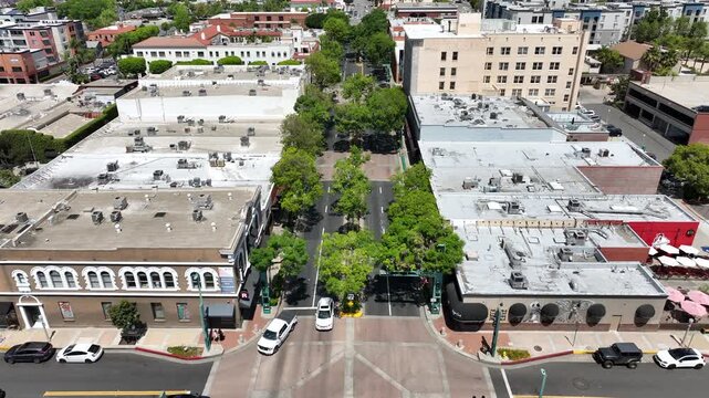 Urban aerial drone shot flying backwards of Harbor Boulevard in Fullerton featuring commercial buildings, outdoor dining, bars, tourists, and active city street traffic in the downtown district.