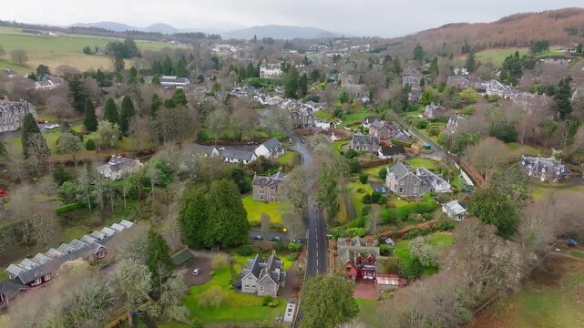 Aerial drone footage over Strathpeffer village, Scottish Highlands, overcast day, Victorian architecture, wooded valley, moody grey sky, Ross-shire, Scotland