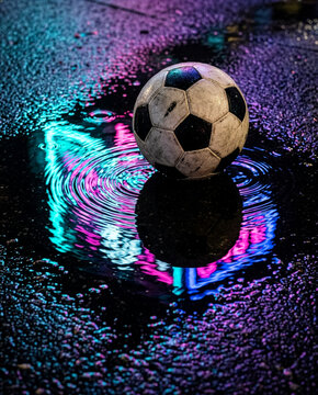 Glossy soccer ball on a wet urban surface, reflecting the Manhattan skyline and stadium lights at night, shallow depth of field, neon blues and warm ambers, photorealistic_l