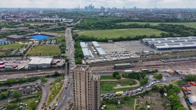Drone hyperlapse over Eastway and New Spitalfields Market toward A12 and City of London skyline, with traffic flow, rail lines, moving trains, and fast clouds.